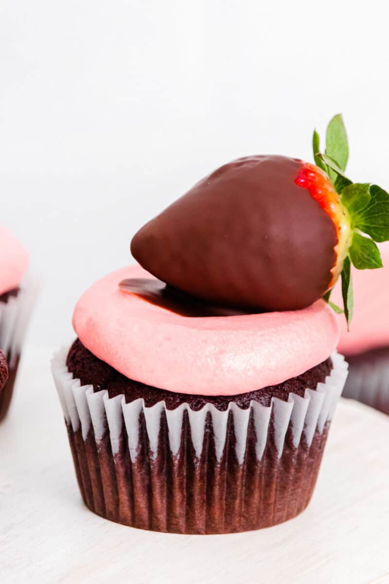 up close image of chocolate cupcake with strawberry frosting and a chocolate covered strawberry