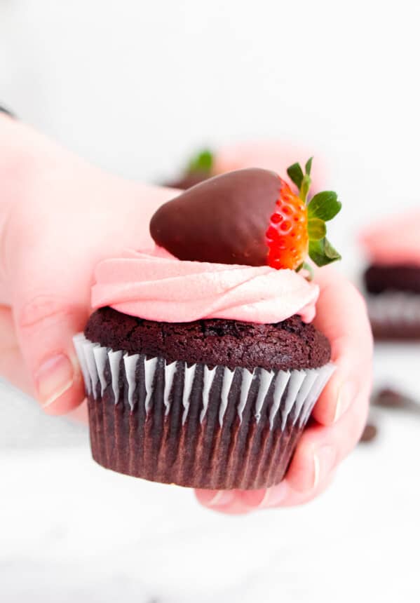 hand holding up chocolate covered strawberry cupcake