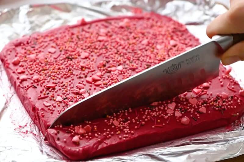 slicing sprinkle-topped red velvet fudge with a knife.