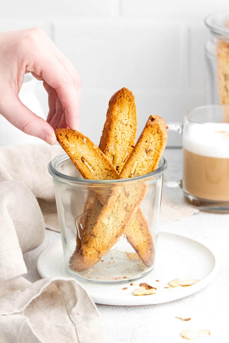 hand lifting out 3 almond biscotti in glass cup