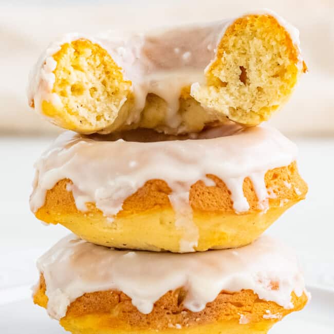 bite out of vanilla glazed baked donuts. three donuts stacked.