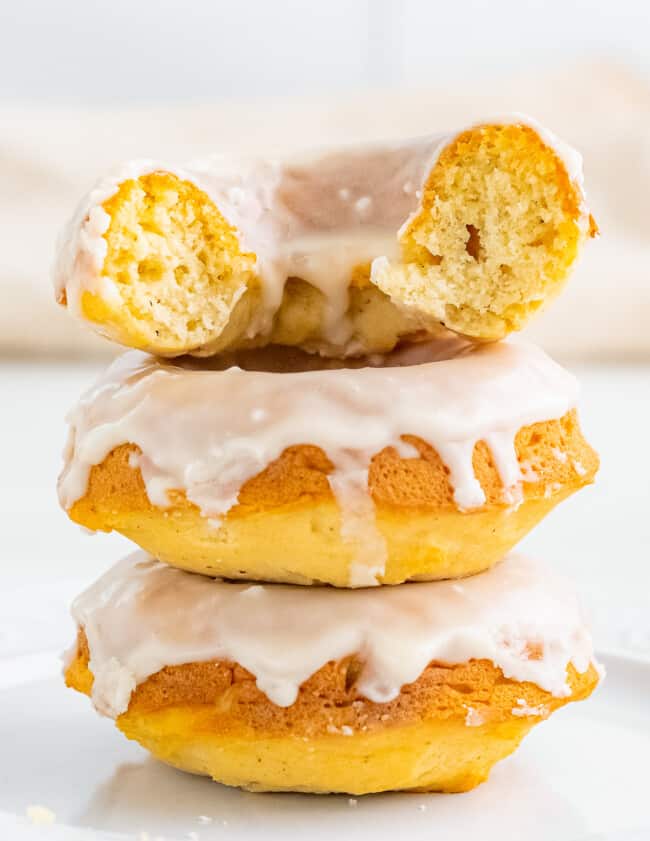 bite out of vanilla glazed baked donuts. three donuts stacked.