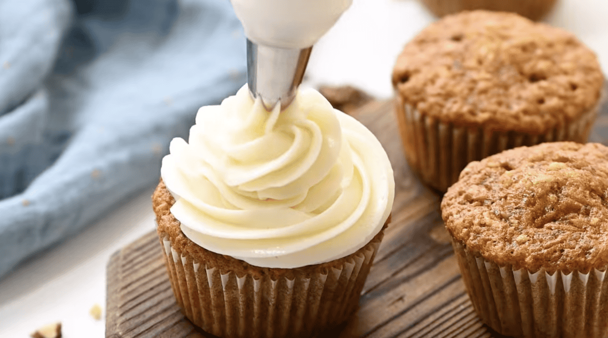 frosting a carrot cake cupcake with cream cheese frosting.