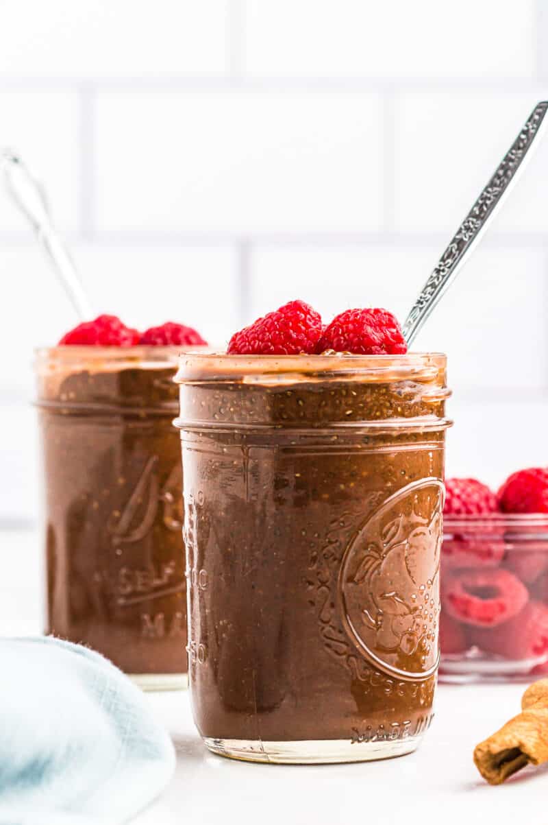two jars of chocolate chia pudding garnished with raspberries