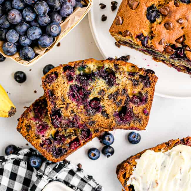 two stacked slices of chocolate chip blueberry banana bread on table next to blueberries