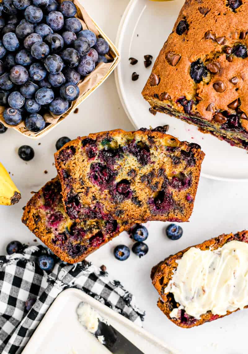 two stacked slices of chocolate chip blueberry banana bread on table next to blueberries