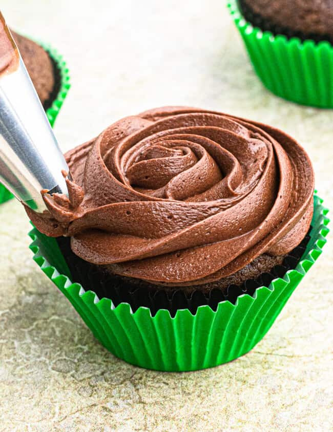 piping chocolate cream cheese frosting on cupcake