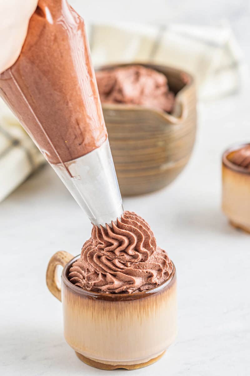 piping chocolate whipped cream frosting into a mug