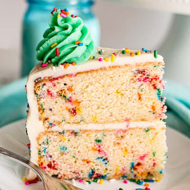 slice of funfetti cake with green frosting on white plate