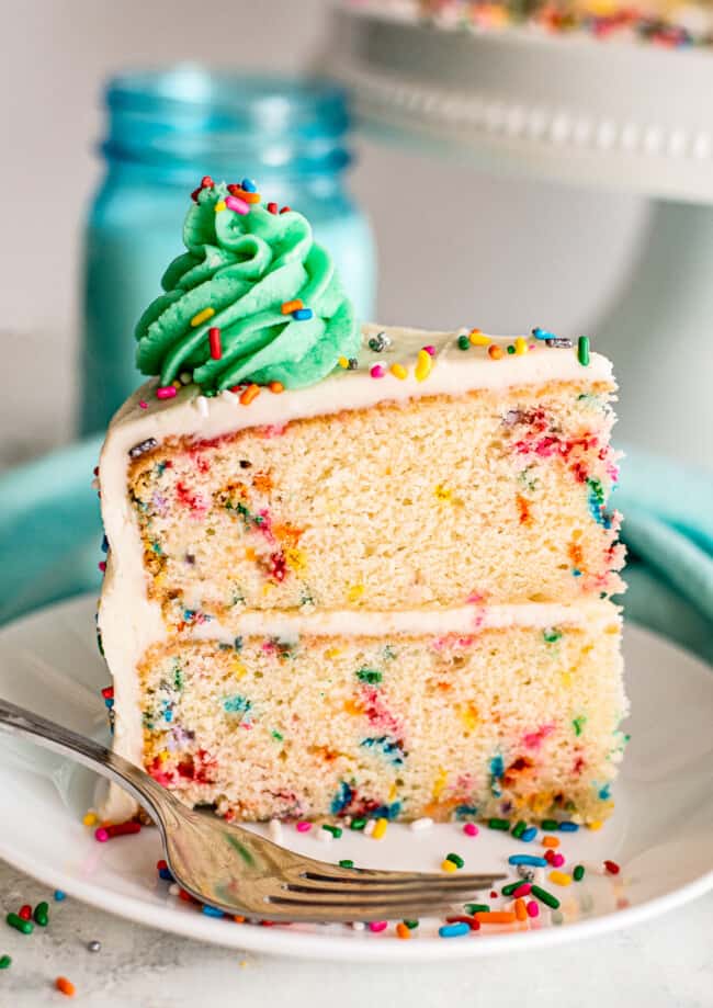slice of funfetti cake with green frosting on white plate