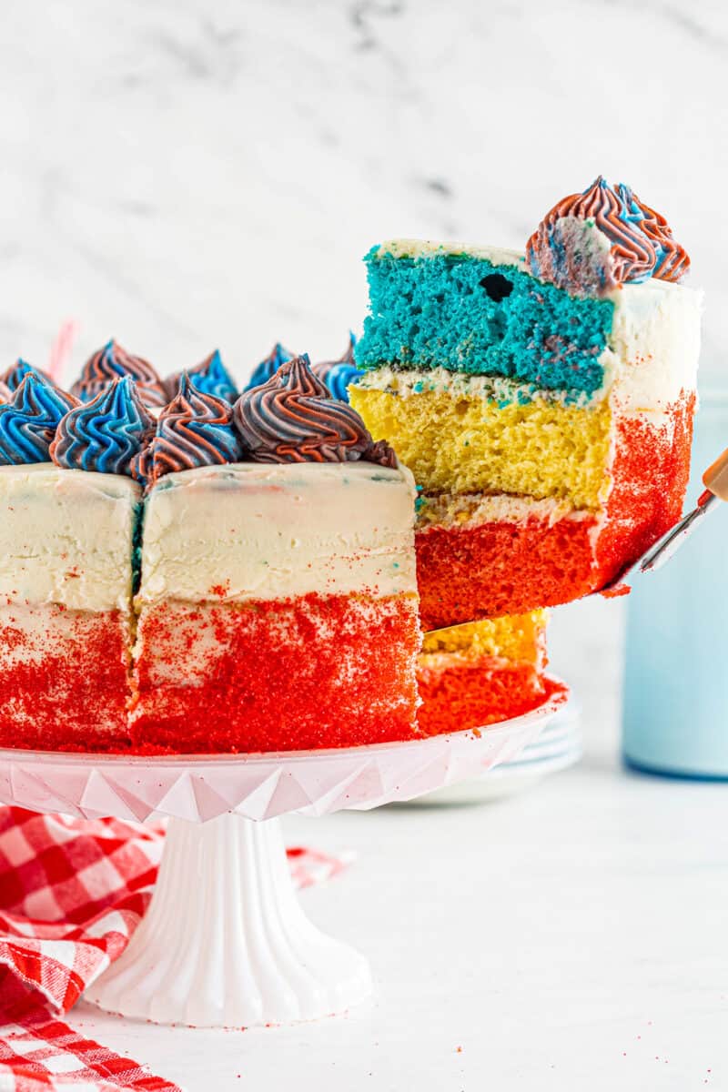 lifting up slice of 4th of july layer cake with red white and blue layers