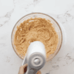 beating peanut butter and butter in a glass bowl with a hand mixer.