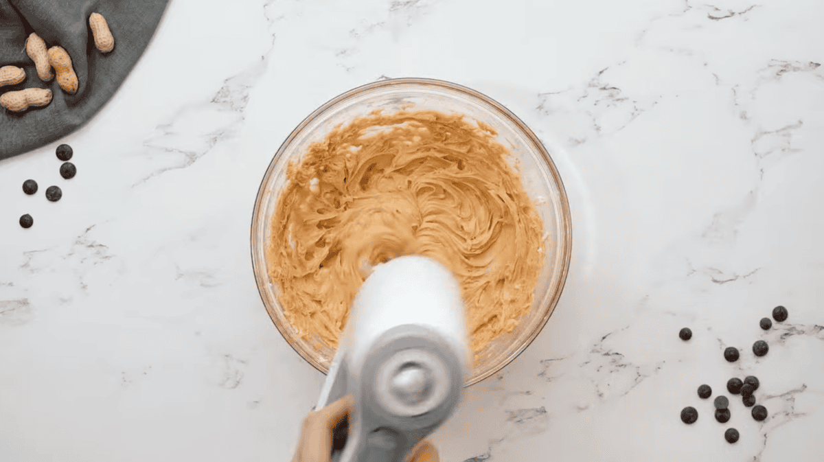 beating peanut butter and butter in a glass bowl with a hand mixer.