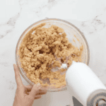 crumbly peanut butter mixture in a glass bowl with a hand mixer.