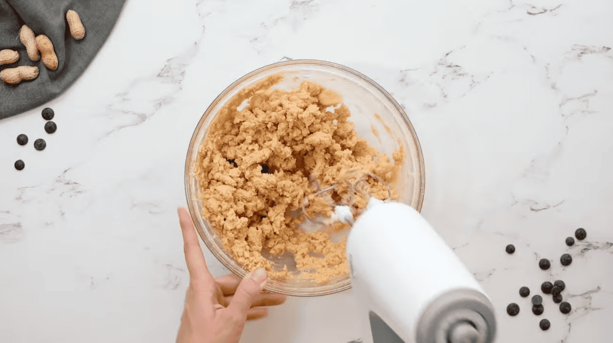 crumbly peanut butter mixture in a glass bowl with a hand mixer.