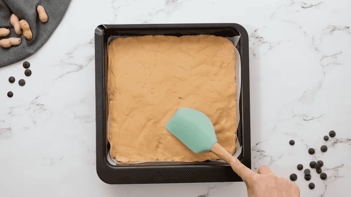 spreading peanut butter mixture into a baking pan wit a rubber spatula.