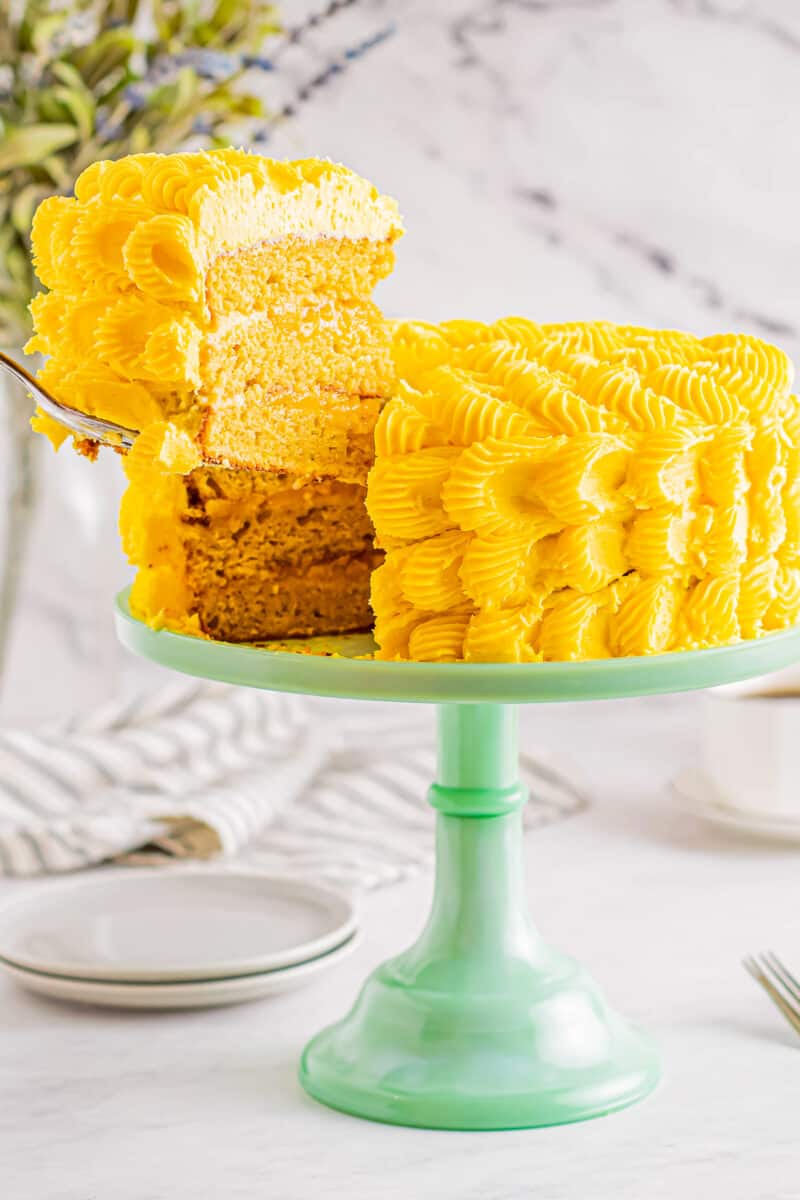iced mango cake on a cake stand with slice out