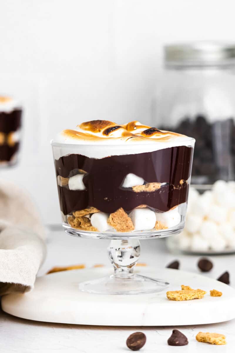 layered smores trifle in glass dish with ingredients in back