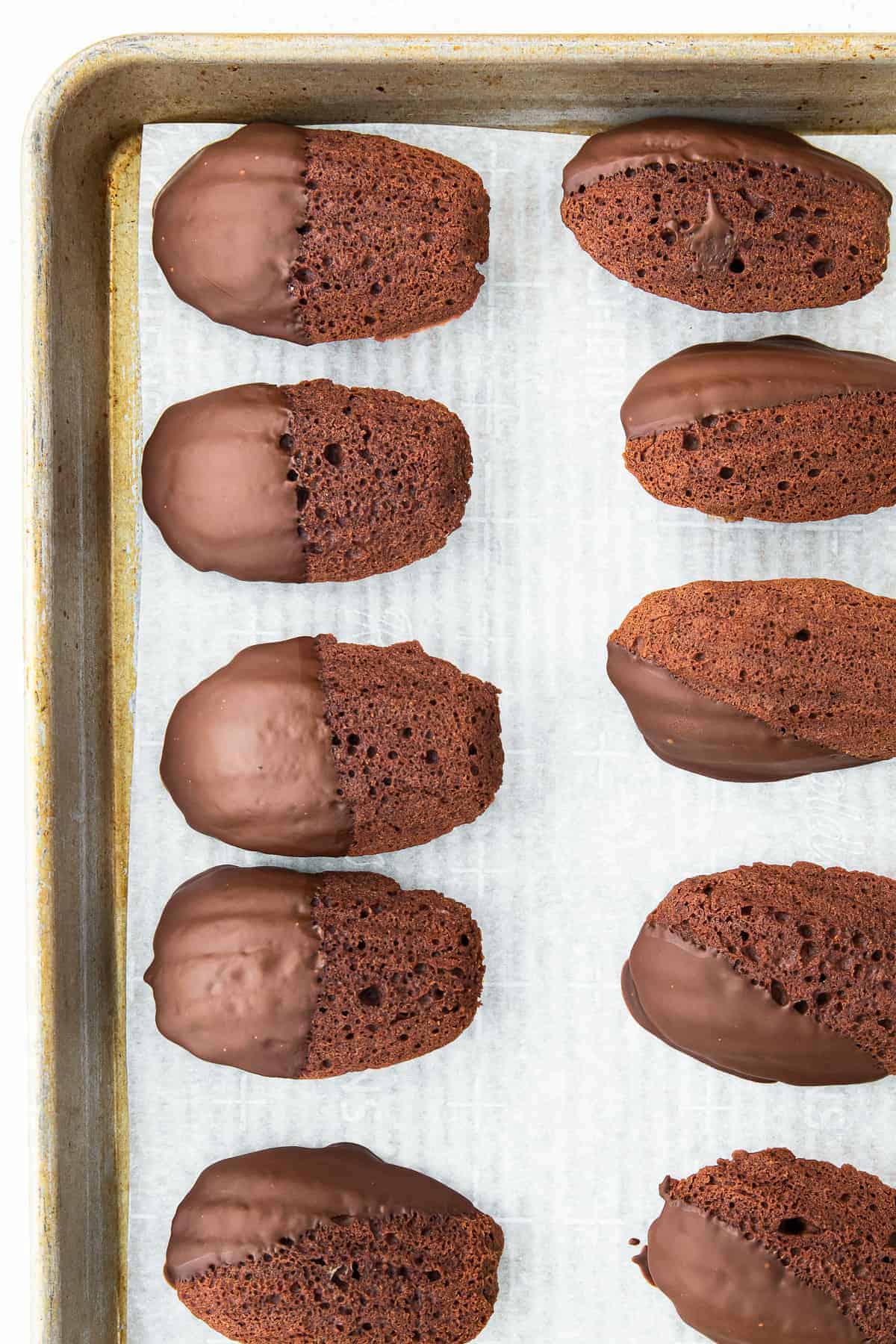 chocolate dipped chocolate madeleine cookies on baking sheet