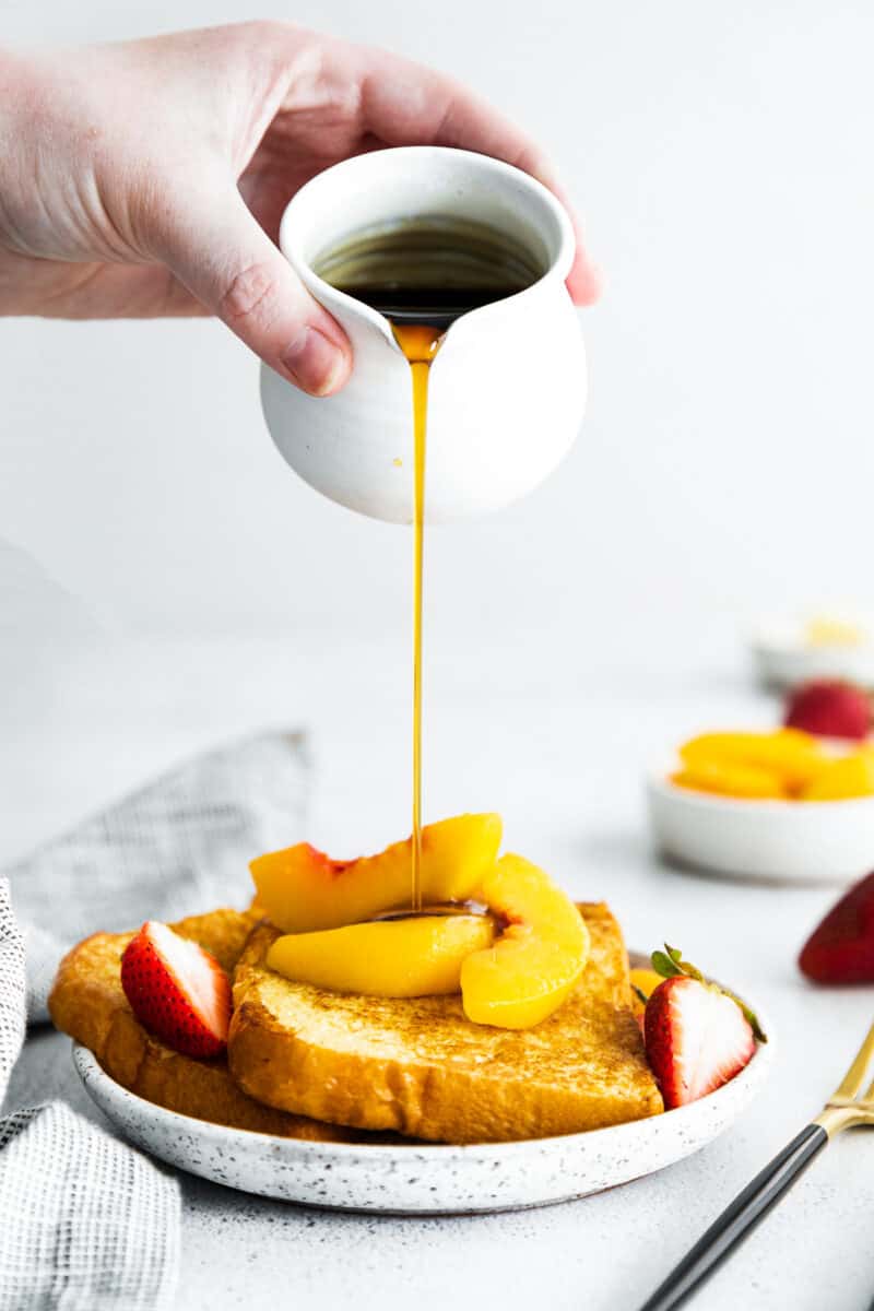 pouring syrup on peach french toast on white plate