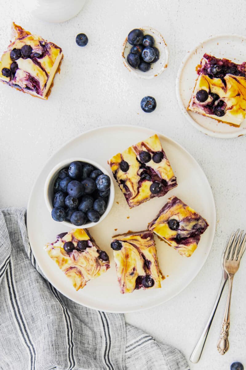 overhead image of 4 blueberry cheesecake bars on a white plate