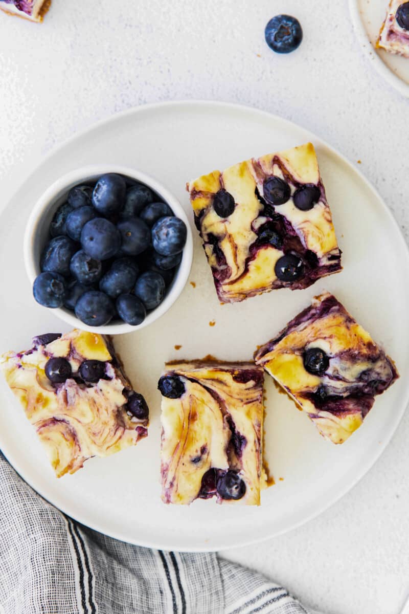 overhead image of 4 blueberry cheesecake bars on a white plate