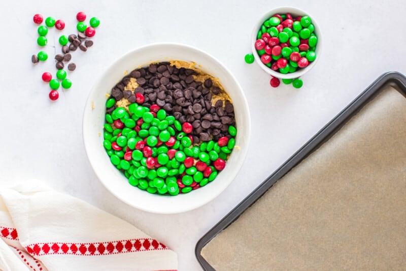 chocolate chips and M&Ms on top of cookie dough in a bowl
