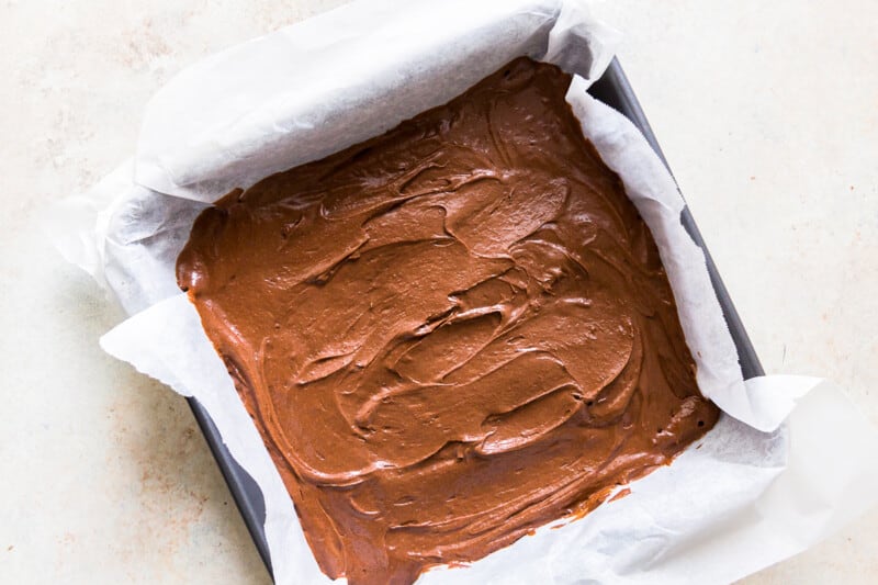 brownie batter in a parchment paper lined square pan before baking