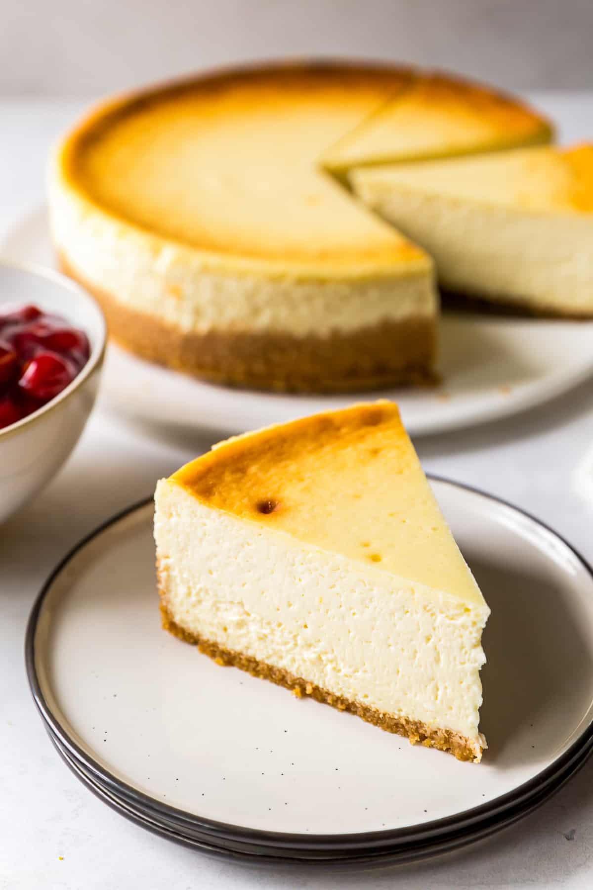 slice of new york style cheesecake with bowl of cherries
