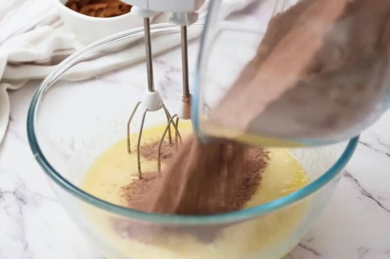 pouring dry chocolate cupcake ingredients into wet with a hand mixer.