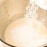 flour being added to wet ingredients for cinnamon sugar donuts in a stainless steel bowl.