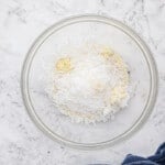 shredded coconut in a glass bowl on a marble countertop.