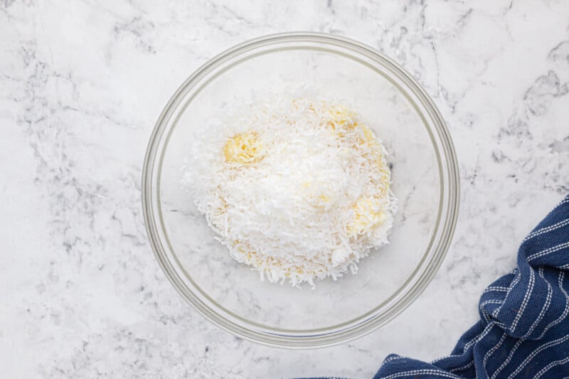 shredded coconut in a glass bowl on a marble countertop.