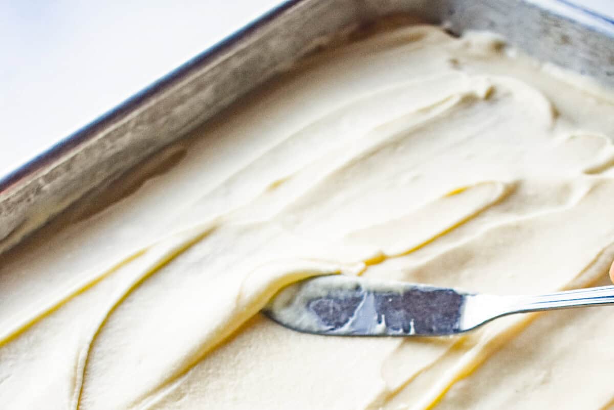 frosted eggnog sheet cake in a 9x13 pan with an offset spatula.