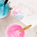 pink and blue marshmallow mixtures being added to a white rectangular pan.