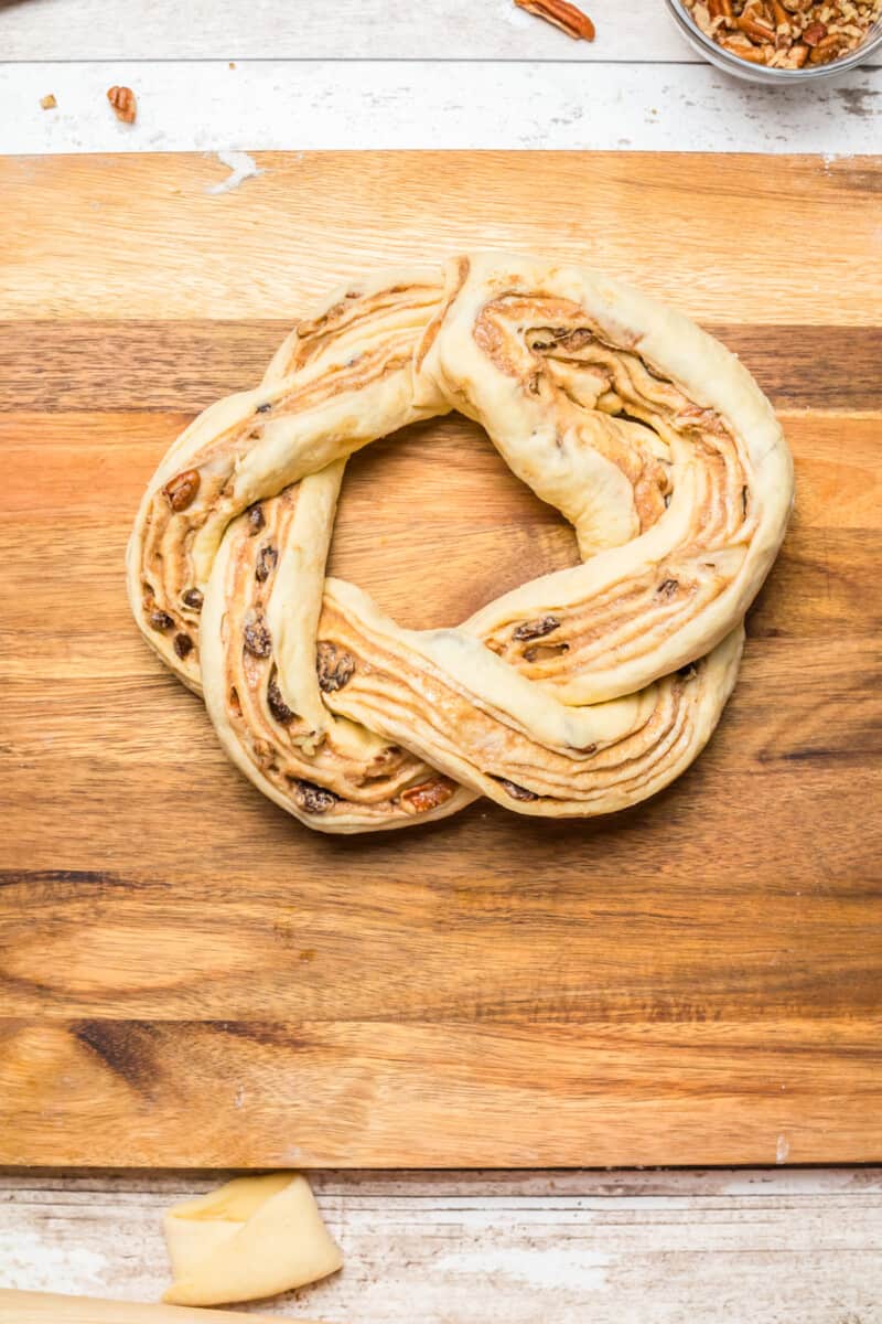 braided estonian kringle dough in a wreath shape on a wood cutting board.