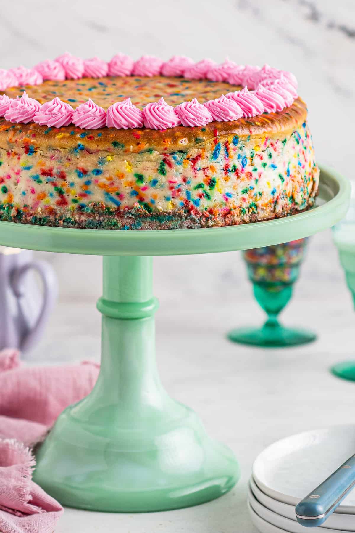 funfetti cheesecake with pink frosting on cake stand