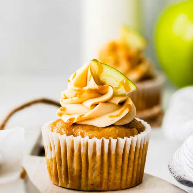 apple cupcakes topped with caramel frosting, a drizzle of salted caramel, and an apple slice