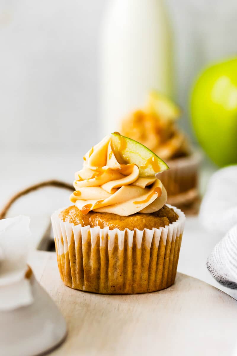 apple cupcakes topped with caramel frosting, a drizzle of salted caramel, and an apple slice