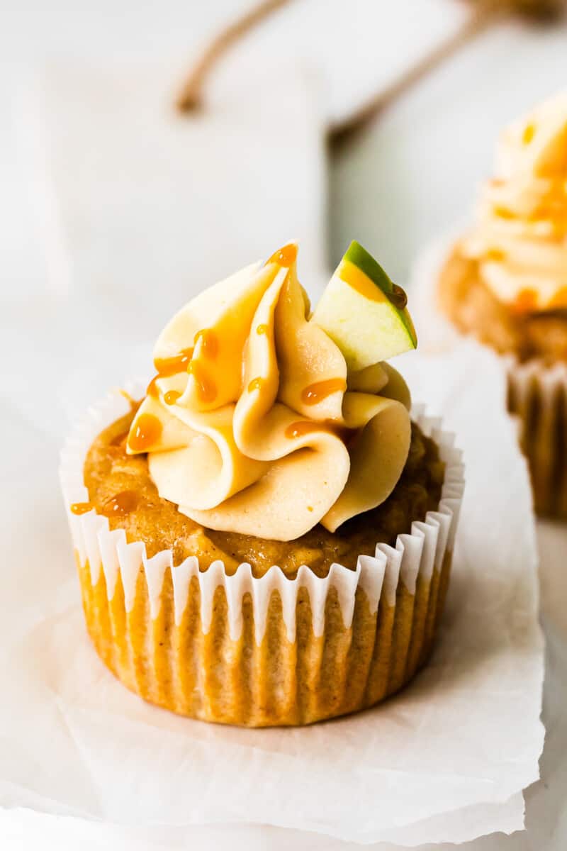 close up of apple cupcake topped with caramel frosting, a drizzle of salted caramel, and an apple slice