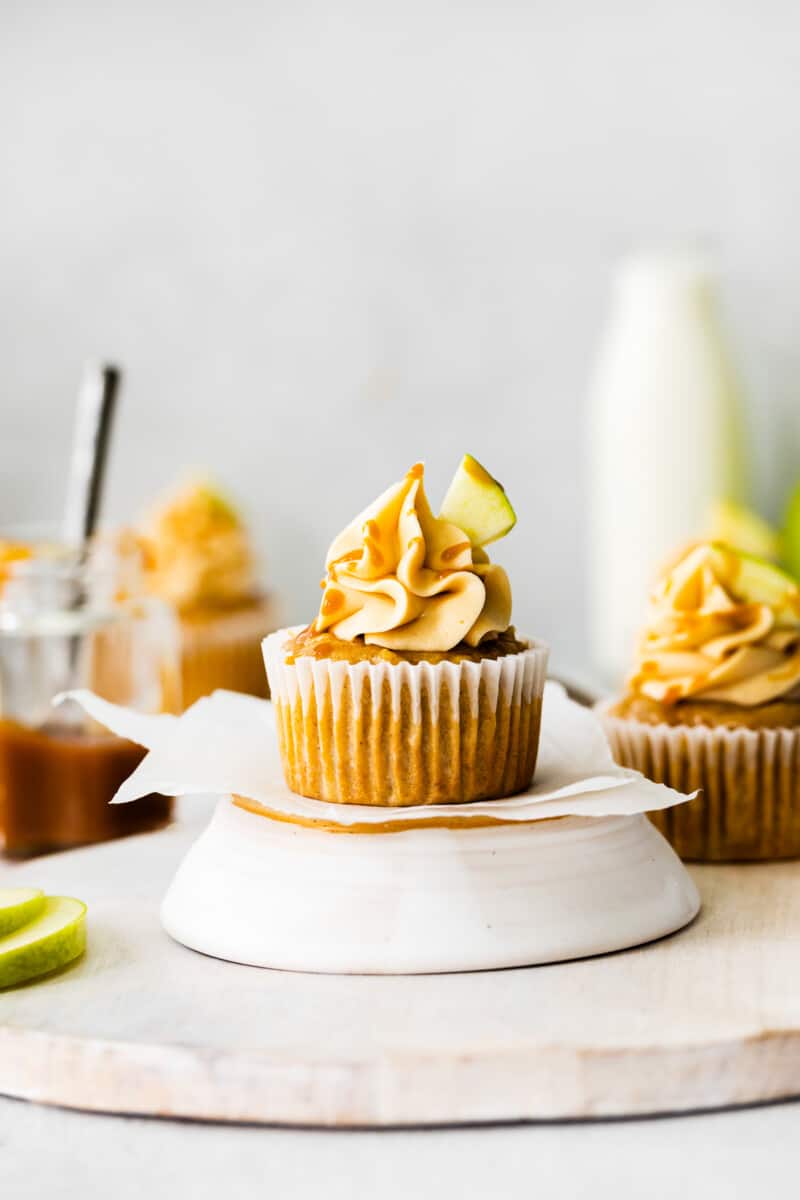 apple cupcake topped with caramel frosting, a drizzle of salted caramel, and an apple slice