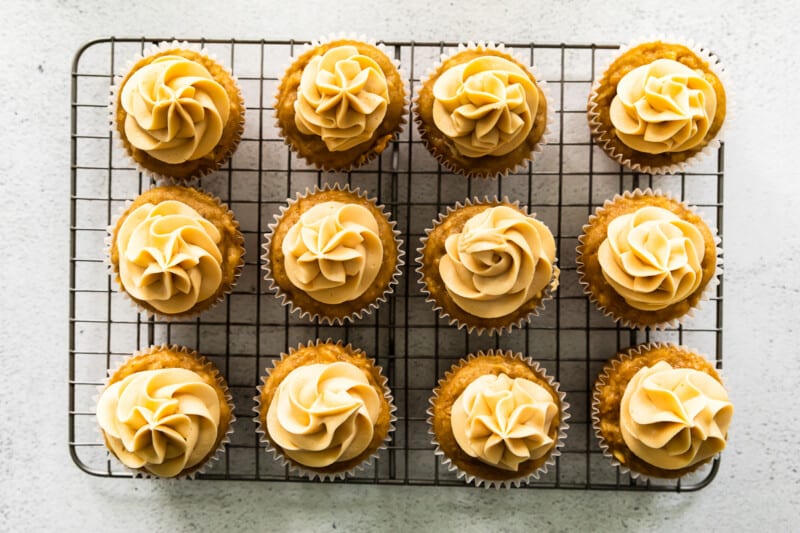 overhead image of 12 apple cupcakes topped with caramel frosting on a cooling rack