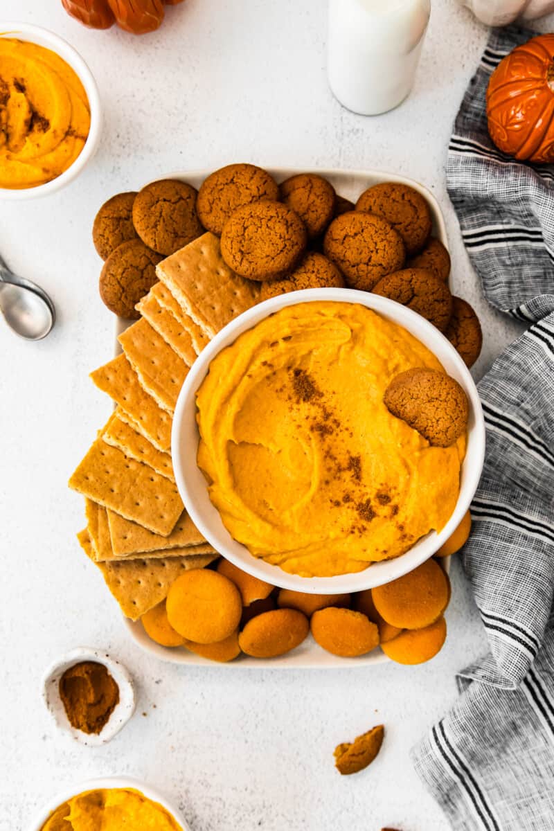 overhead image of pumpkin cheesecake dip in a white bowl on a platter with vanilla wafers, graham crackers, and gingersnaps