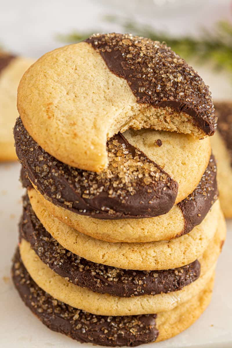stack of sugar cookies with half of each cookie dipped in chocolate with a bite taken from one cookie