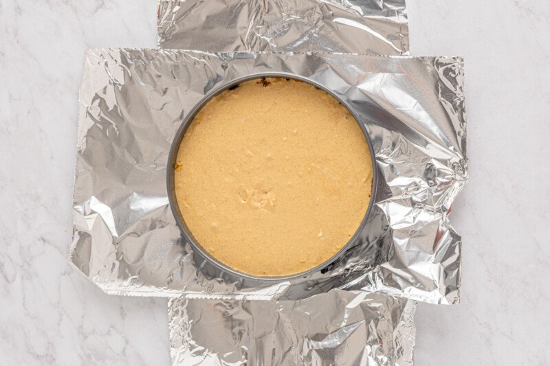 gingerbread cheesecake batter in a springform pan surrounded by aluminum foil.