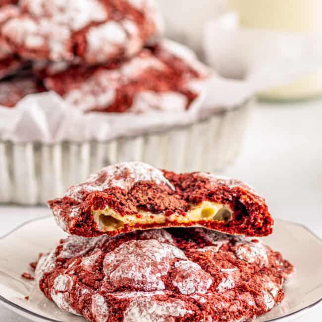 cheesecake stuffed red velvet cookies on a plate with one cookie broken in half showing the filling