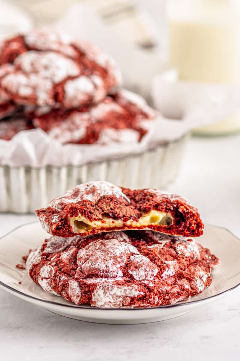cheesecake stuffed red velvet cookies on a plate with one cookie broken in half showing the filling