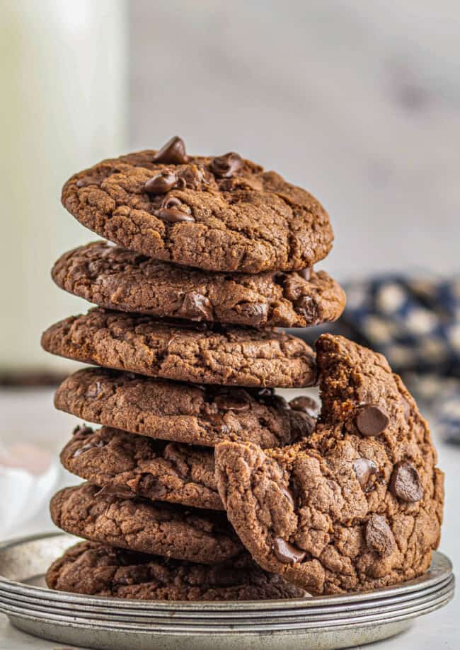 stack of chocolate cookies with chocolate chips with a cookie on the side with a bite taken