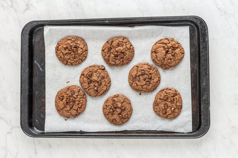 8 chocolate cookies with chocolate chips on a parchment lined baking sheet after baking
