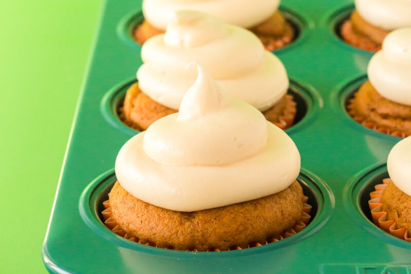 pumpkin cupcakes in a cupcake pan topped with cream cheese frosting